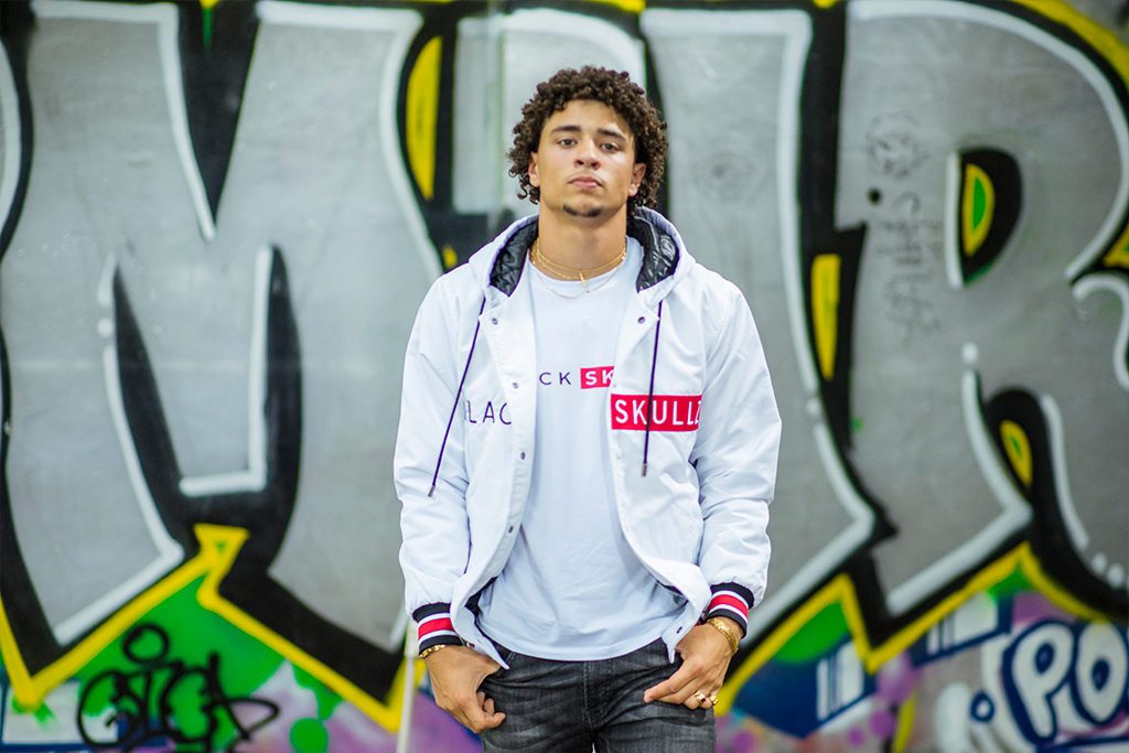 male model wearing white hooded varsity jacket with red and black embroidery and logo