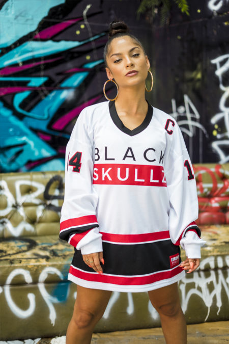female wearing white hockey jersey with blackskullz logo and black and red embroidery