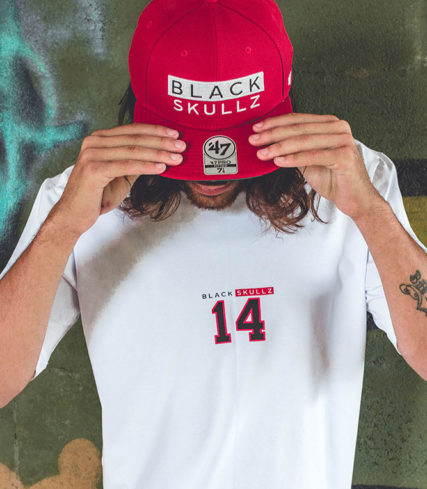 male model wearing red fitted hat with black skullz logo embroidered and brand white tshirt